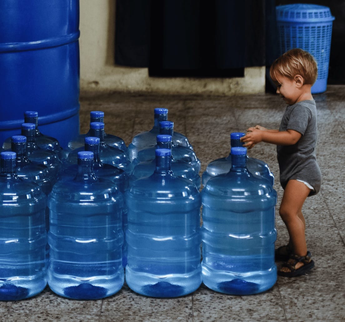 Toddler standing next to 14 5-gallon water containers