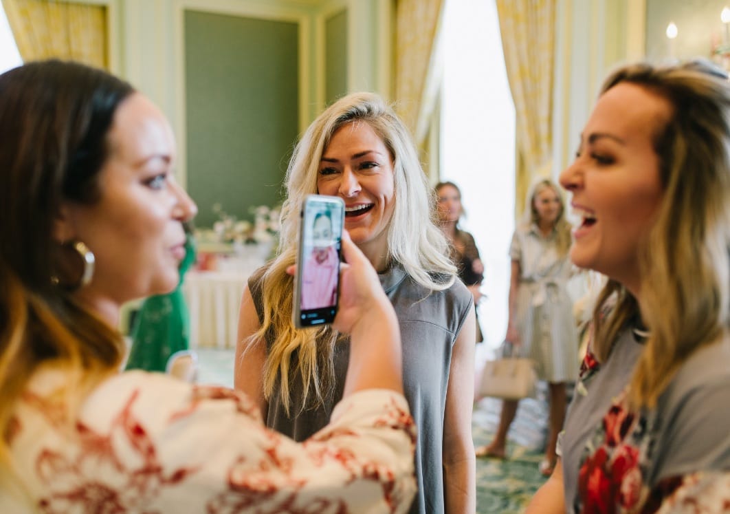 Woman showing picture on smart phone to two smiling women.