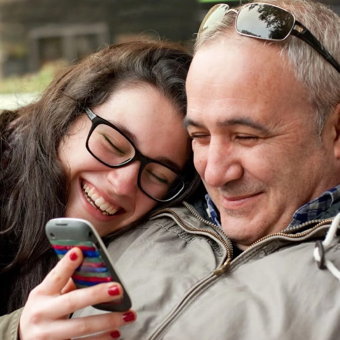 Father and daughter smiling while looking at daughter's mobile phone